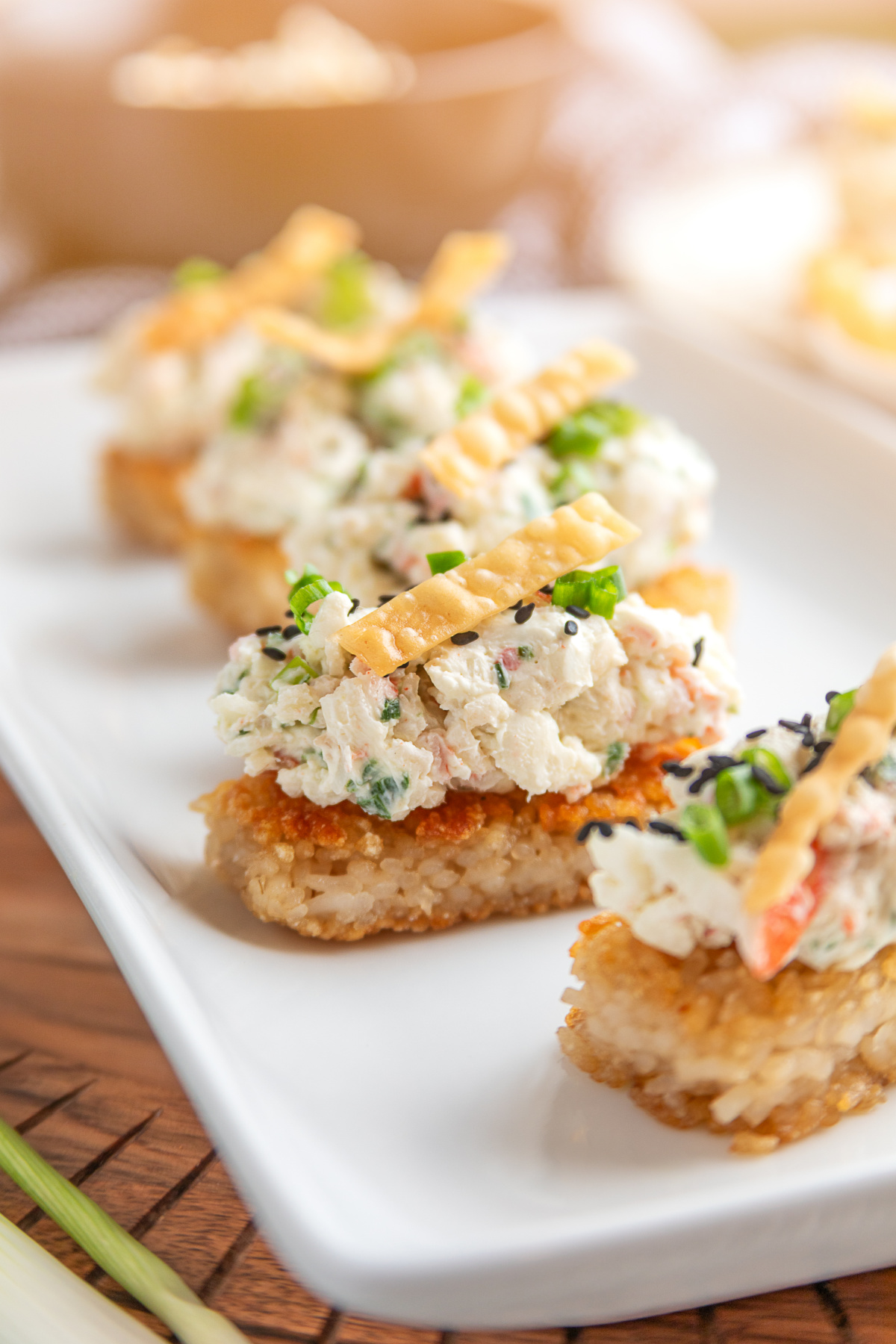 Crispy Rice Crab Rangoon Bites on a serving platter with creamy crab topping, green onions, sesame seeds, and wonton strips