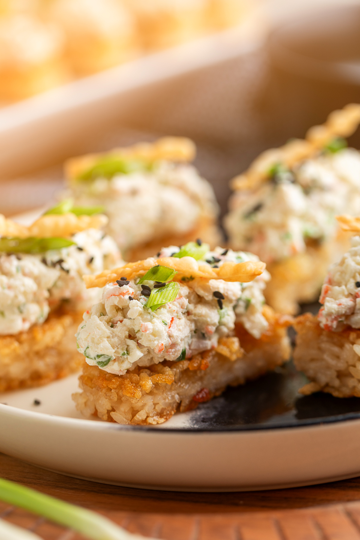 Crispy Rice Crab Rangoon Bites on a plate with creamy crab topping, green onions, sesame seeds, and wonton strips