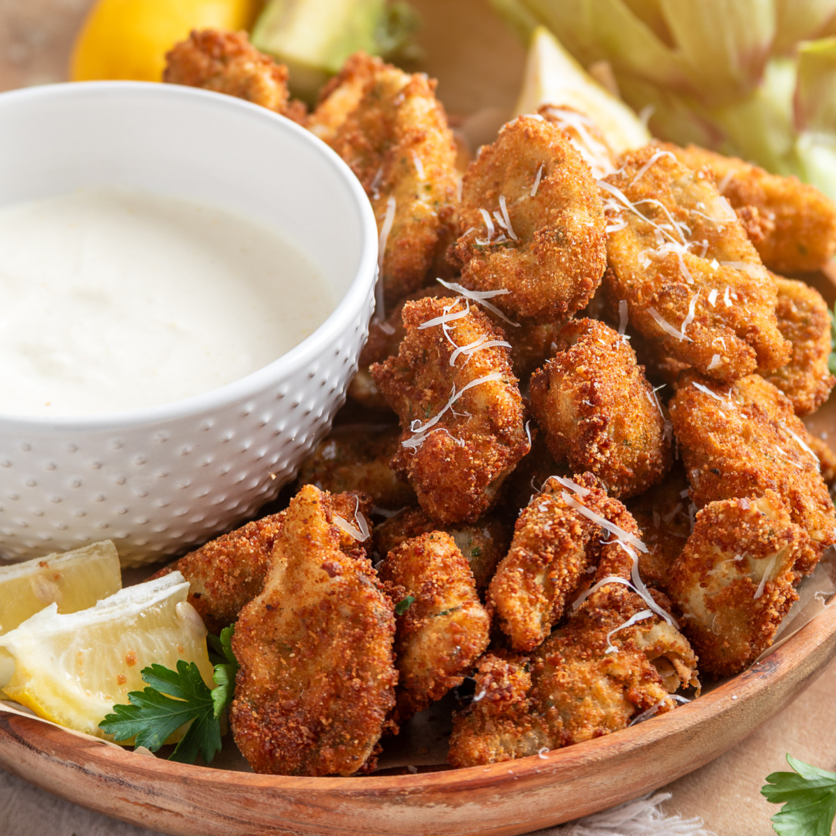 Fried artichokes with lemon garlic aioli on a platter with lemon wedges and Parmesan