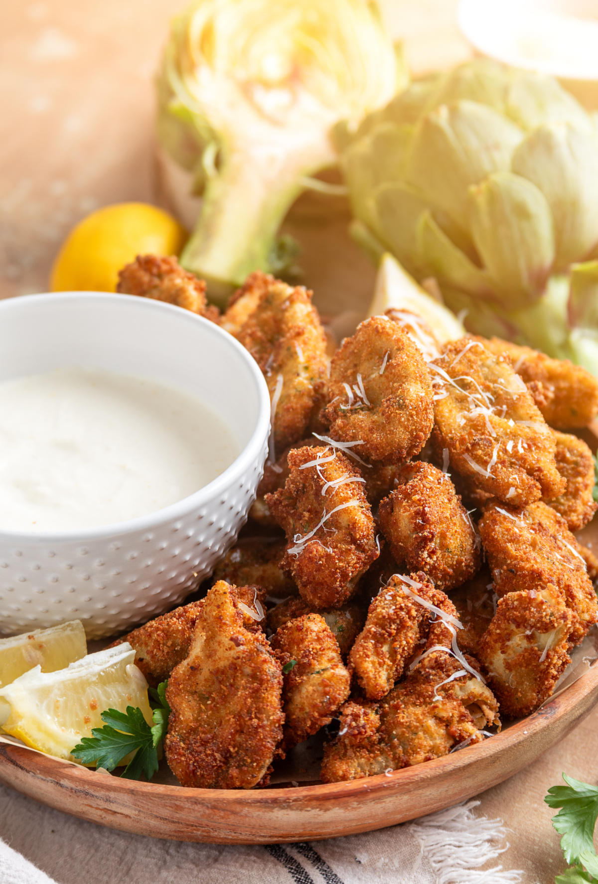Fried artichokes with lemon garlic aioli served on a wooden platter with lemon wedges and grated Parmesan