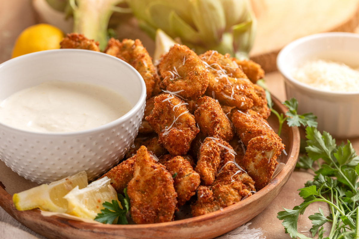 Fried artichokes with lemon garlic aioli on a wooden platter with lemon wedges and parsley