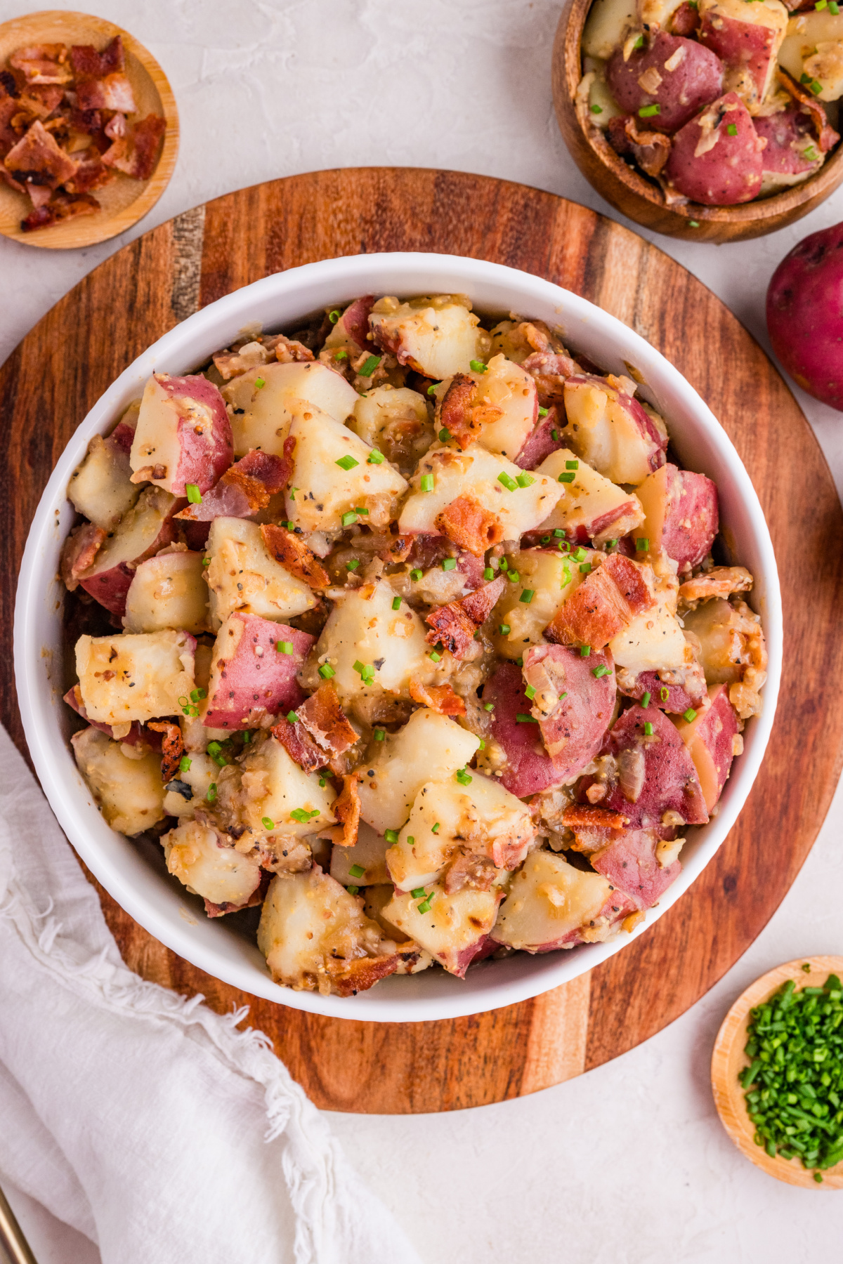 German potato salad with bacon, red potatoes, and mustard dressing in a serving bowl with chives
