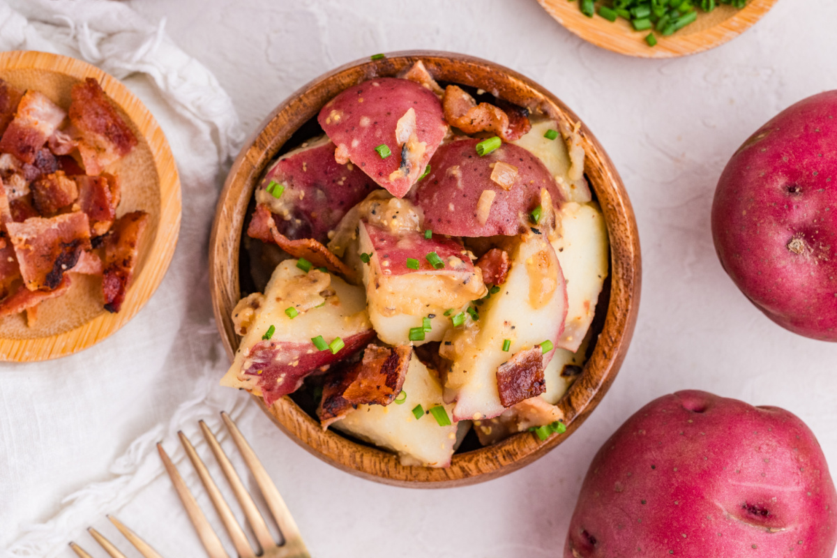 German potato salad with red potatoes, bacon, and mustard dressing served in a wooden bowl with chives