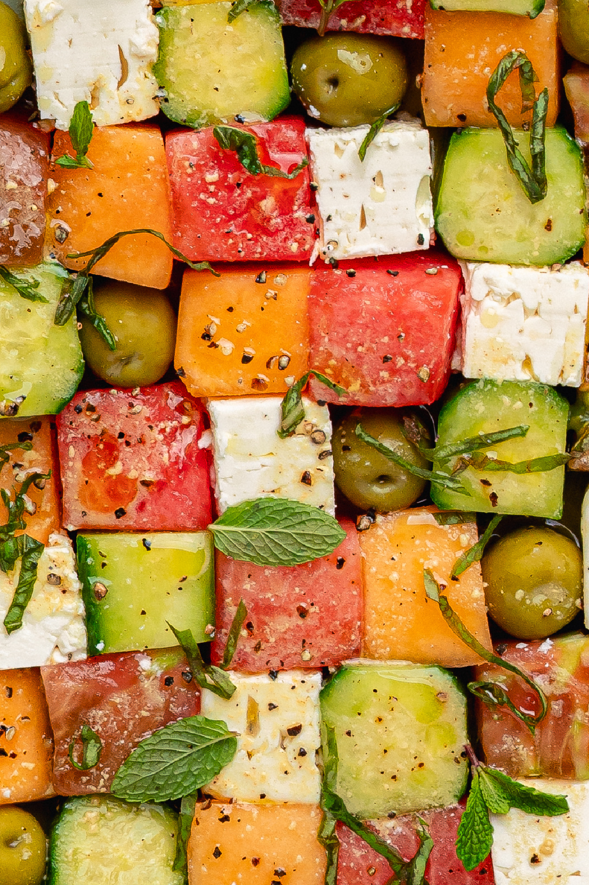 Greek mosaic salad with watermelon, feta, cucumber, olives, and herbs arranged in a colorful pattern