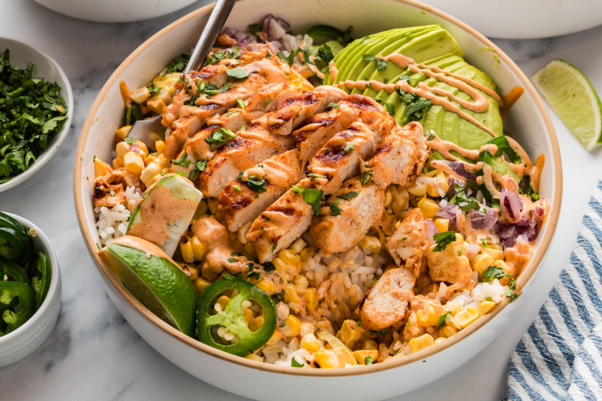 grilled chicken rice bowl with charred corn, avocado slices, jalape&ntilde;os, red onion, and creamy elote-style sauce