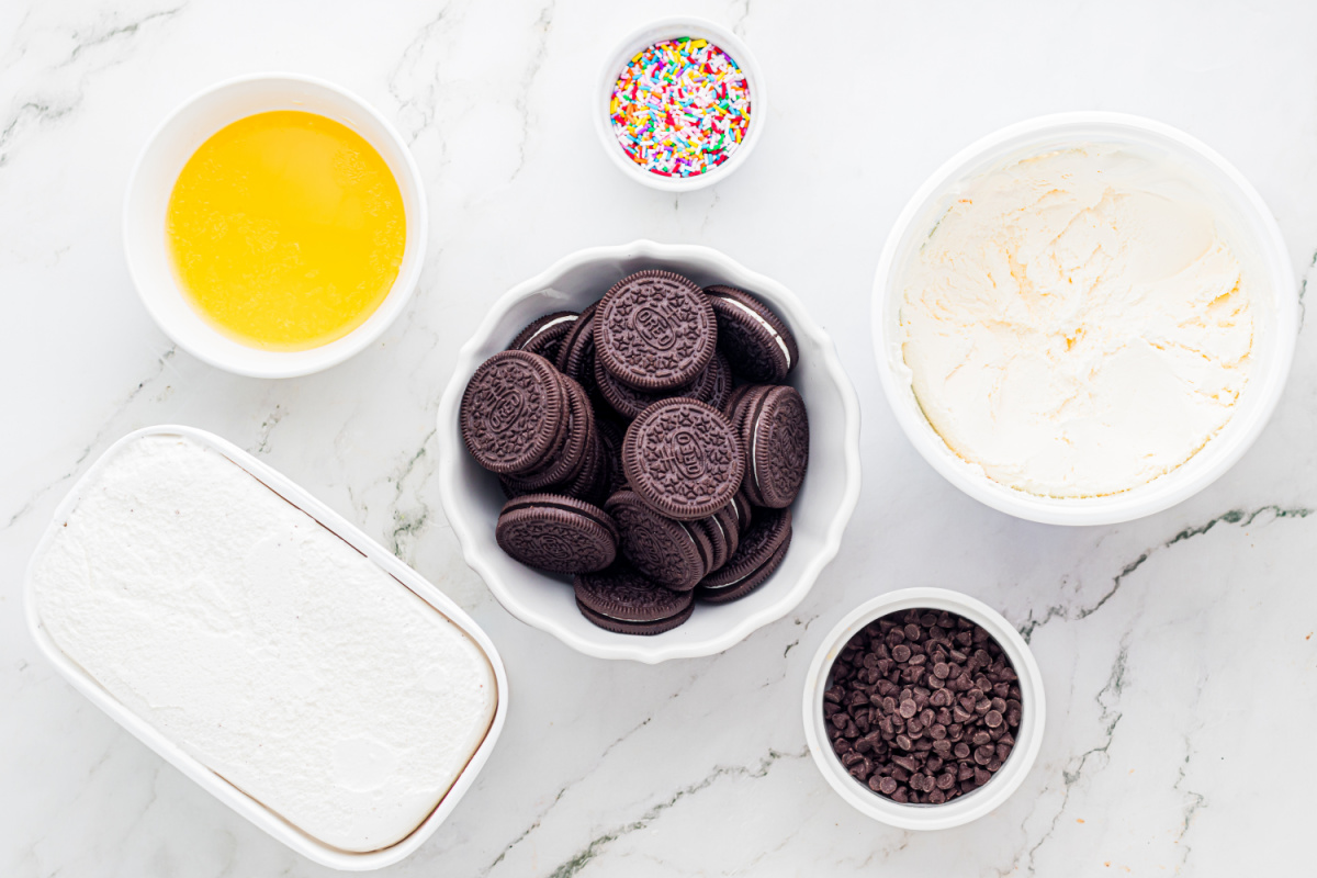 ingredients for Oreo crust ice cream dessert including sandwich cookies, butter, ice cream, sprinkles, and chocolate chips