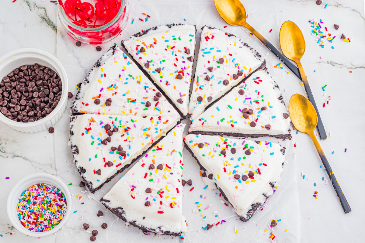 overhead ice cream pizza with Oreo crust cut into slices with sprinkles and chocolate chips
