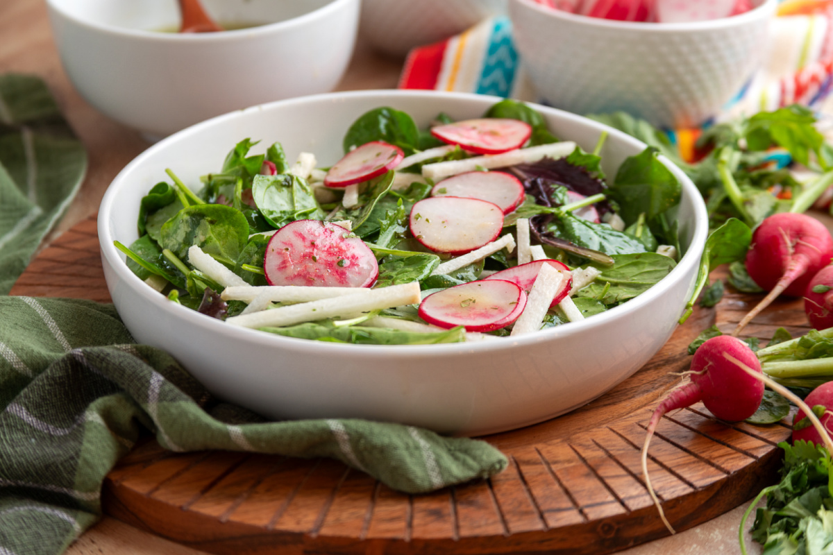 jicama radish salad with mixed greens and lime vinaigrette in a white bowl