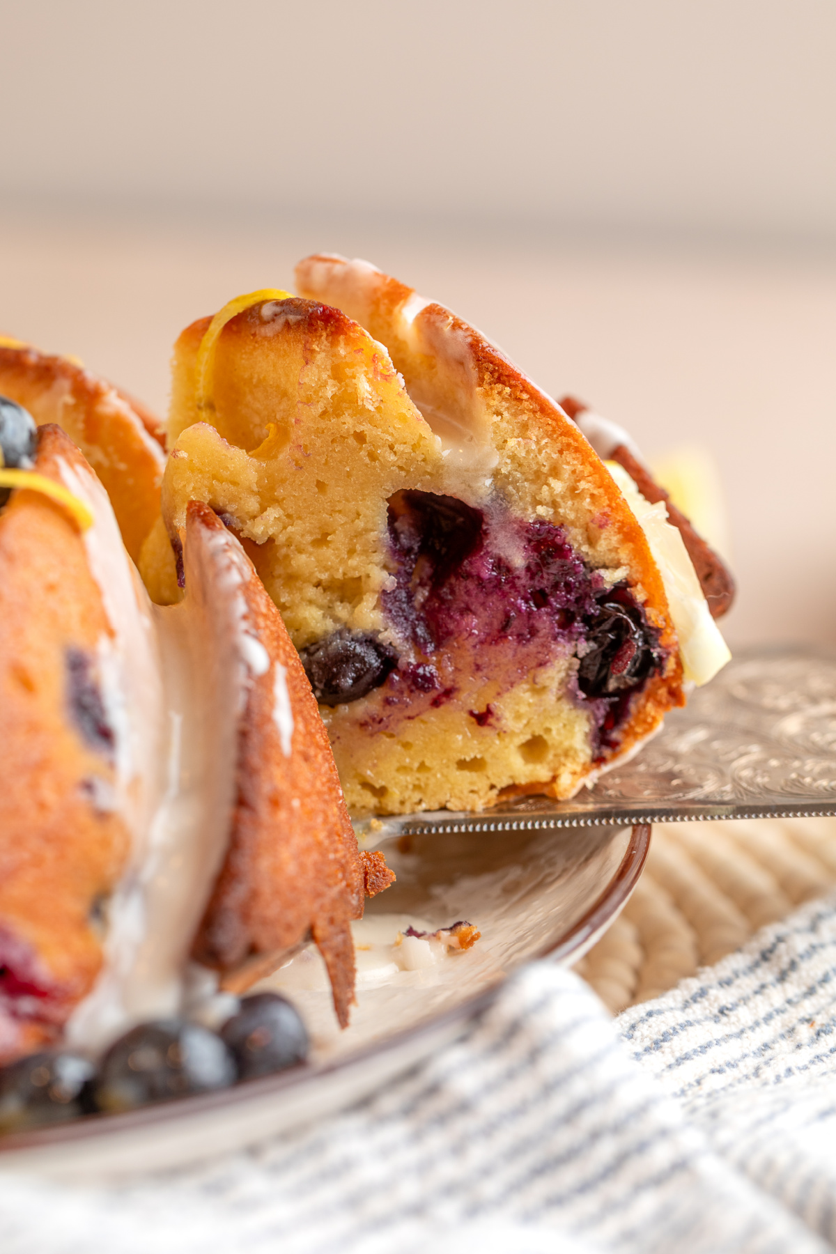 slice of lemon blueberry bundt cake showing interior with baked blueberries and lemon glaze