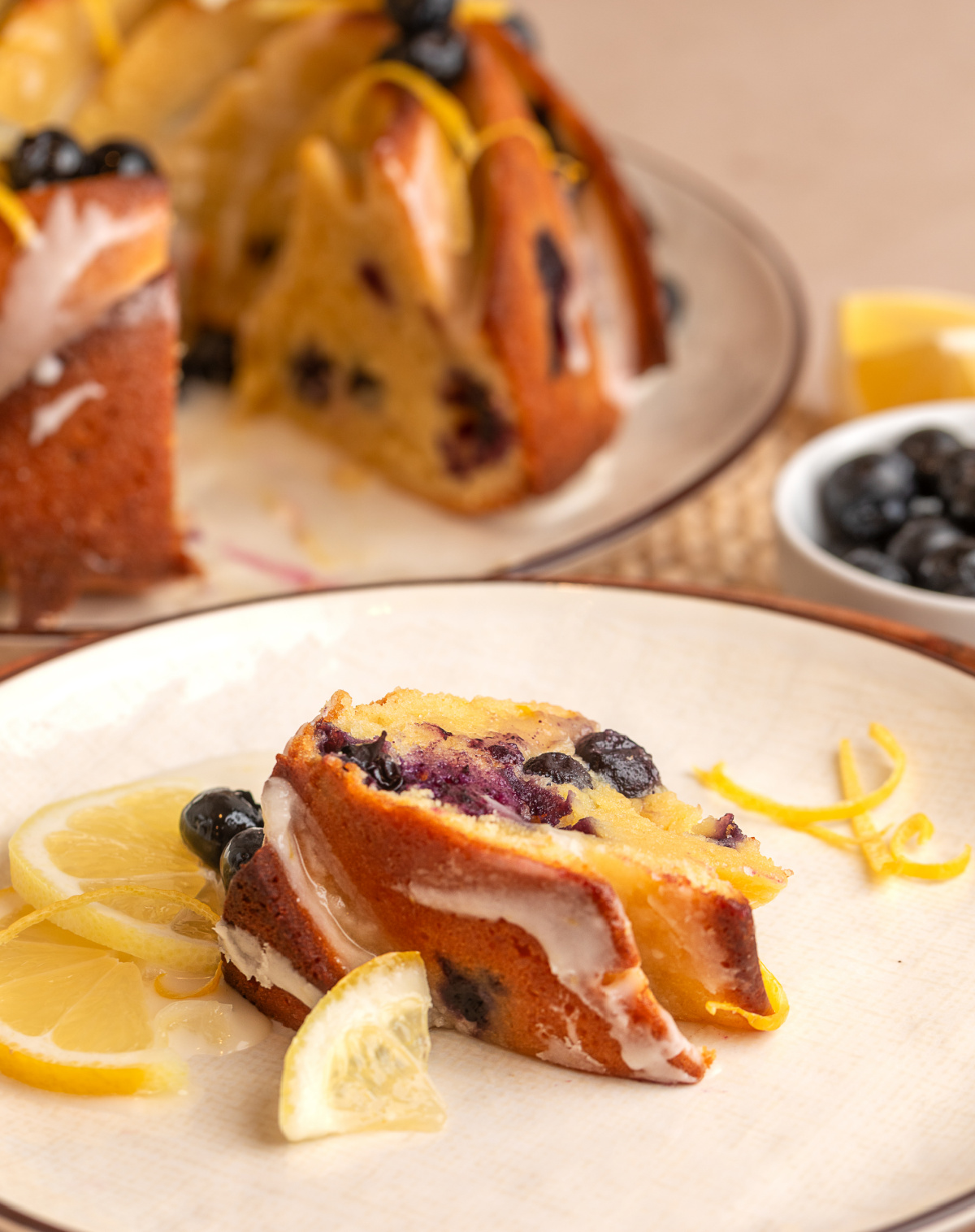 slice of lemon blueberry bundt cake on a plate with glaze, fresh blueberries, and lemon slices