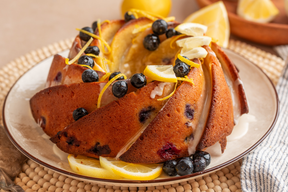 sliced lemon blueberry bundt cake with lemon glaze, fresh blueberries, and lemon slices on a plate
