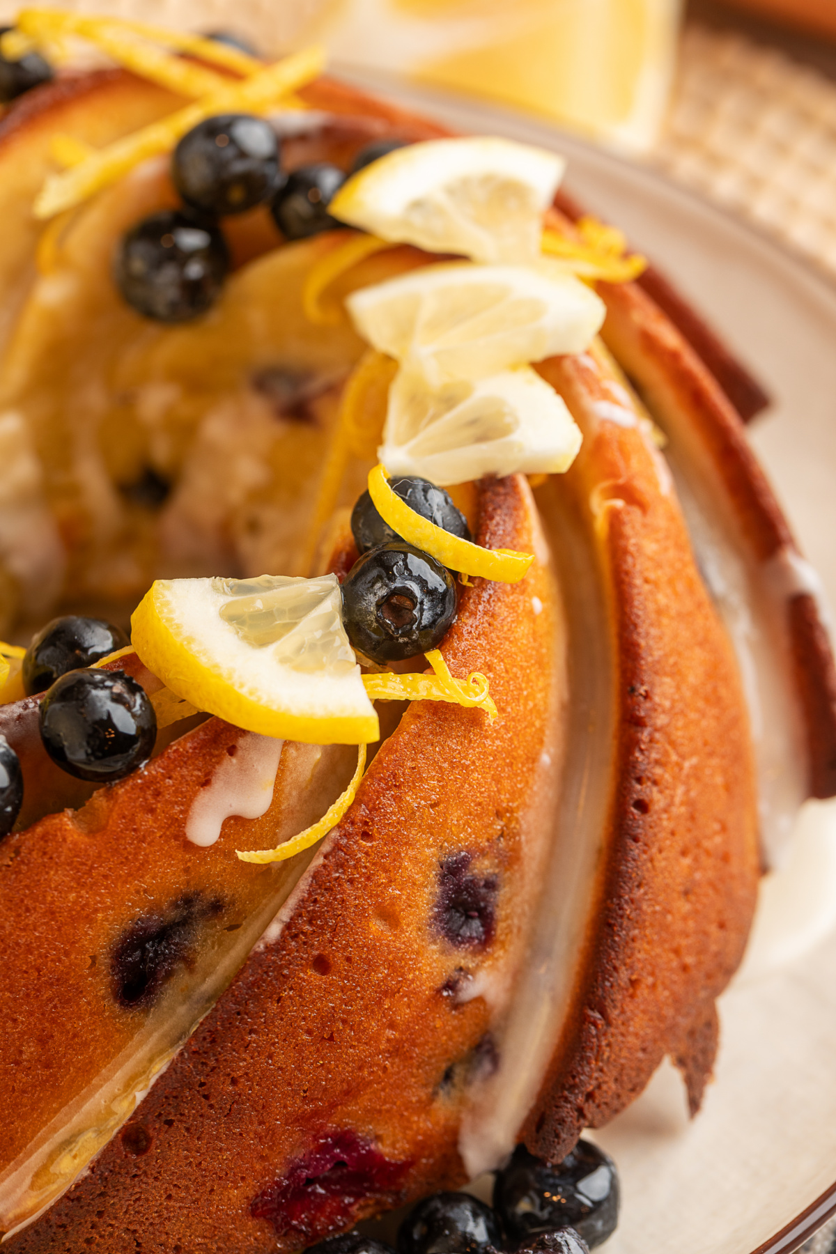 lemon blueberry sour cream bundt cake close up with lemon glaze, blueberries, and lemon slices