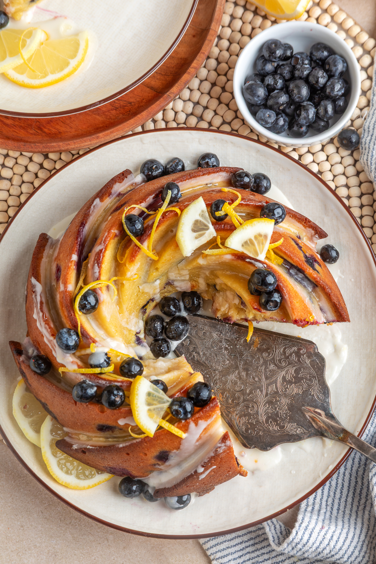lemon blueberry sour cream bundt cake sliced on a plate with glaze, fresh blueberries, and lemon slices