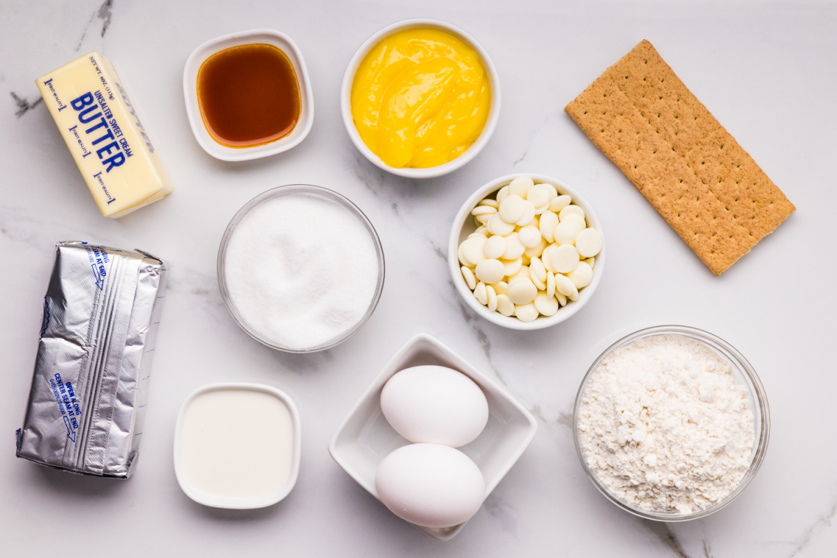 ingredients for lemon cheesecake bars including graham crackers cream cheese eggs lemon curd and white chocolate