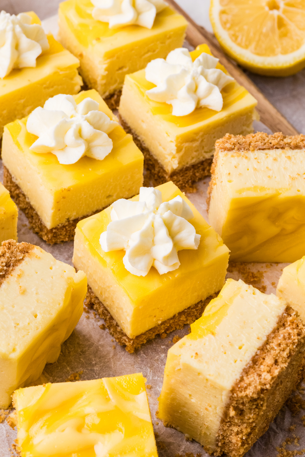 lemon cheesecake bars cut into squares with whipped cream and lemon curd topping