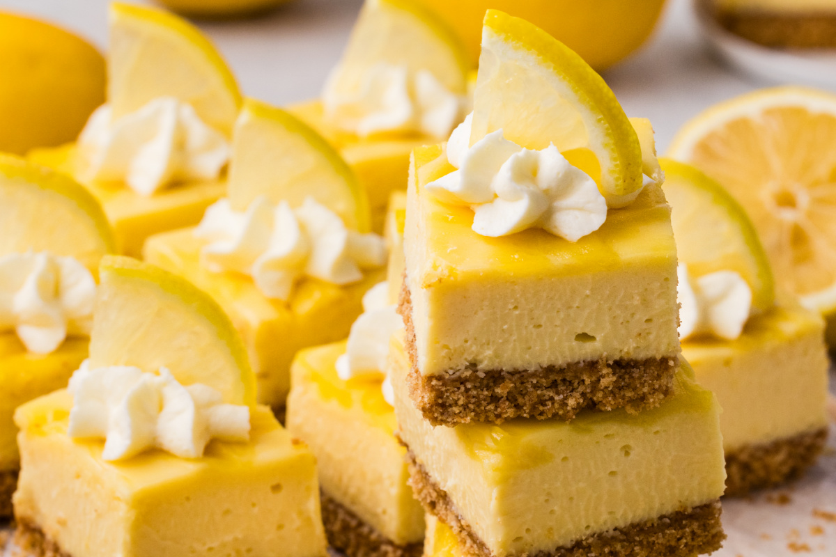 lemon cheesecake bars topped with whipped cream and fresh lemon slices