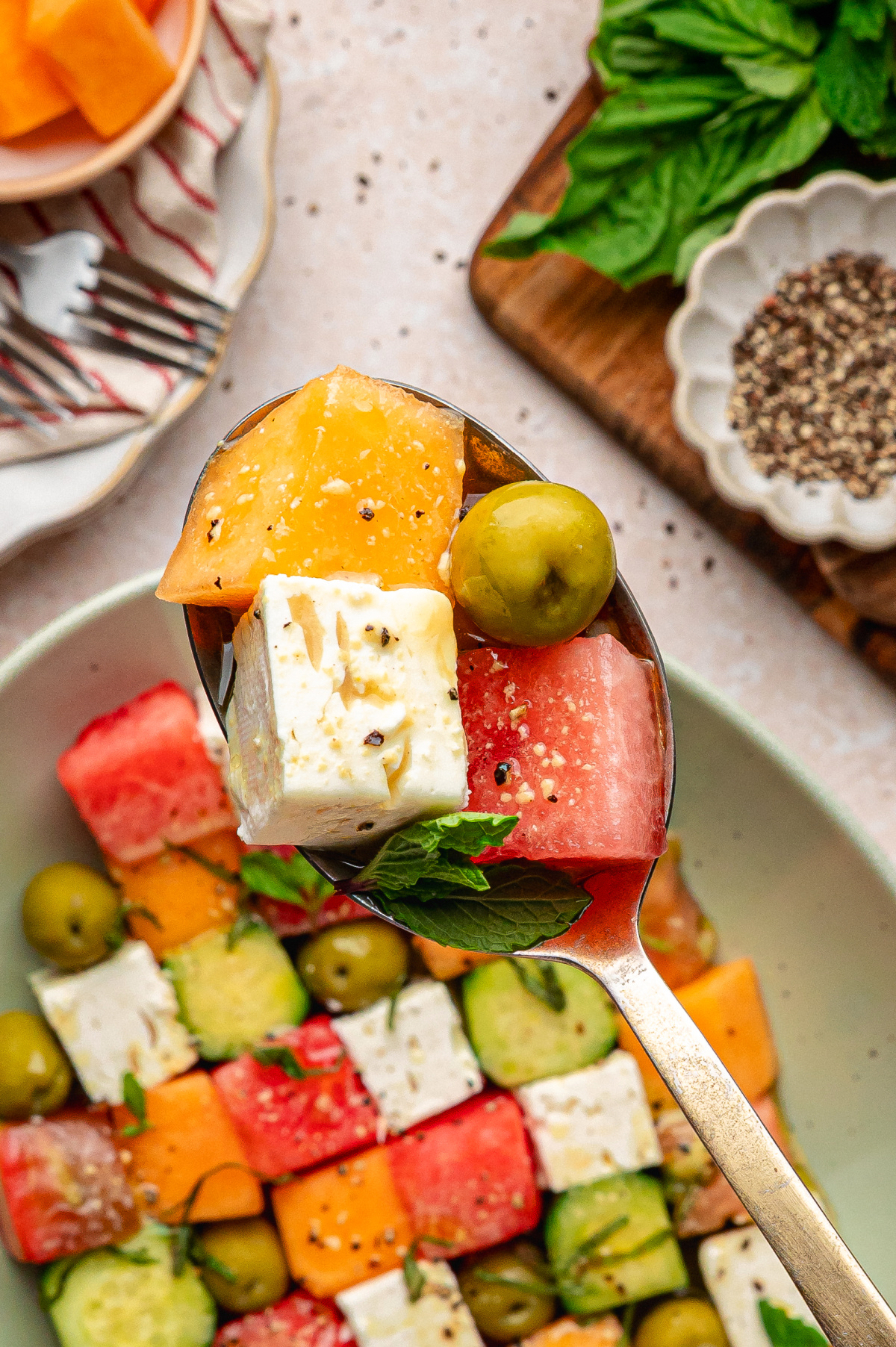 spoonful of melon and feta salad with cucumber, olives, and fresh herbs