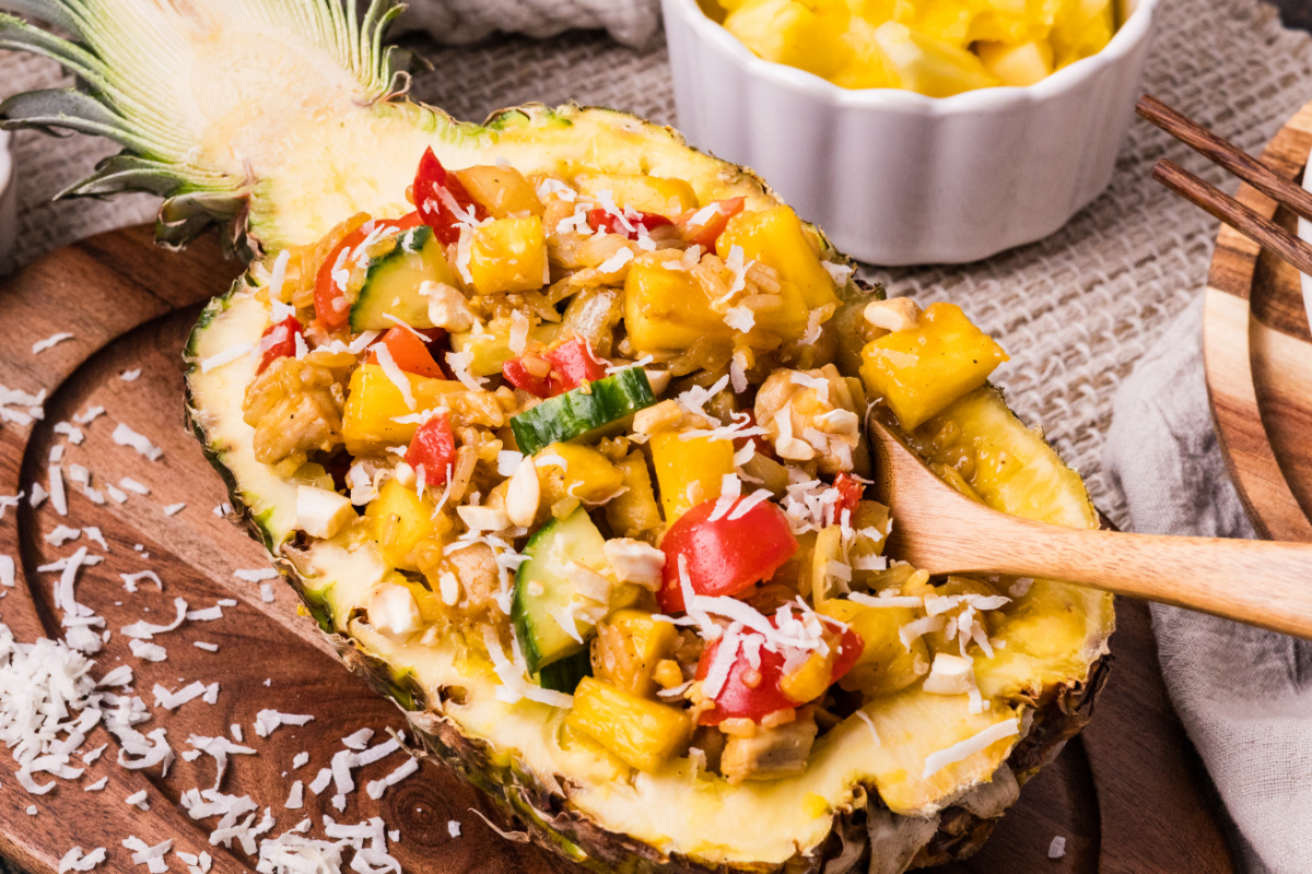 pineapple chicken and rice in a hollowed pineapple with coconut rice, chicken, pineapple, and fresh vegetables