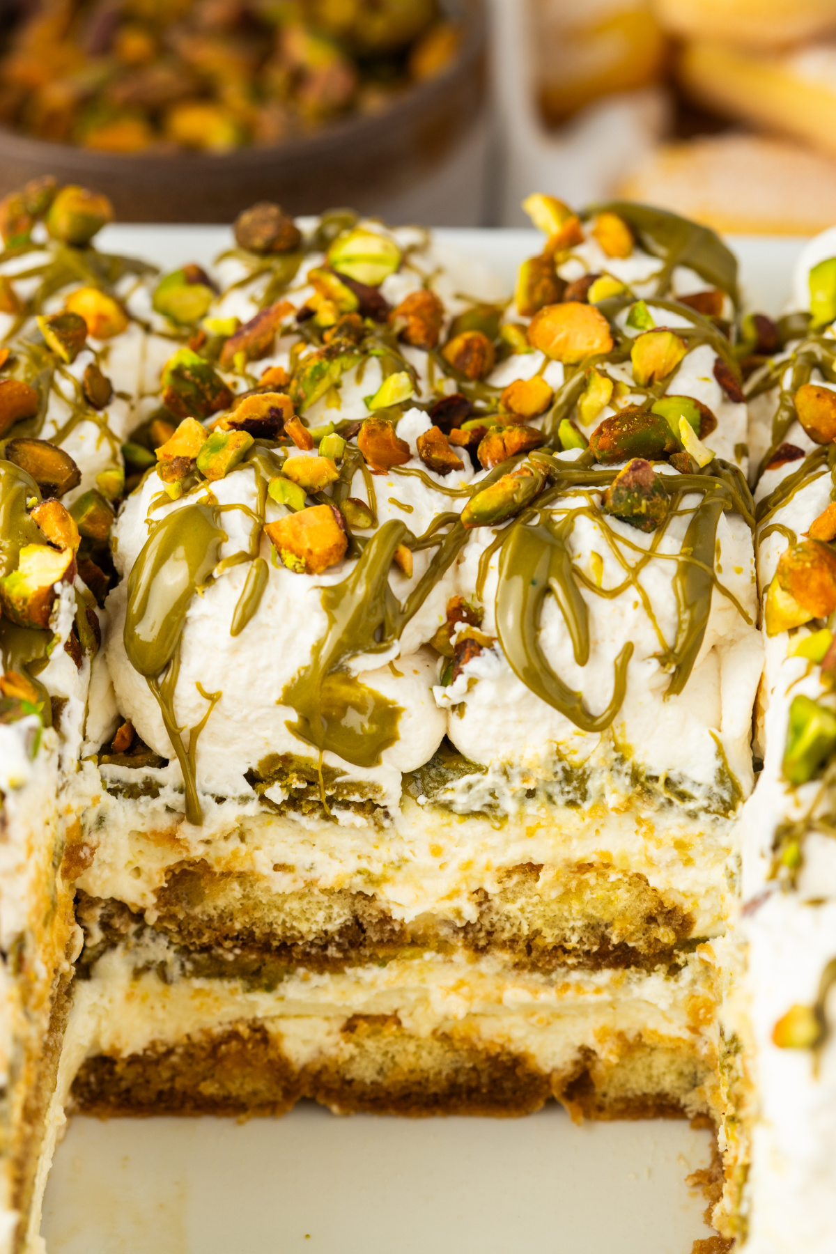 slice of tiramisu showing layers of mascarpone cream espresso soaked ladyfingers and pistachio cream with whipped topping and chopped pistachios