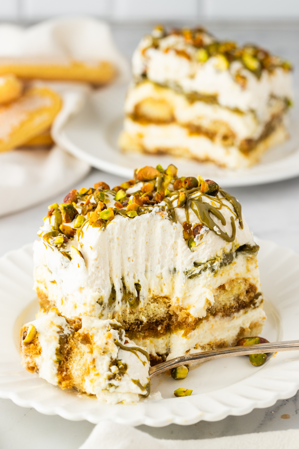 slice of tiramisu with a bite taken showing mascarpone layers espresso soaked ladyfingers and pistachio cream with chopped pistachios