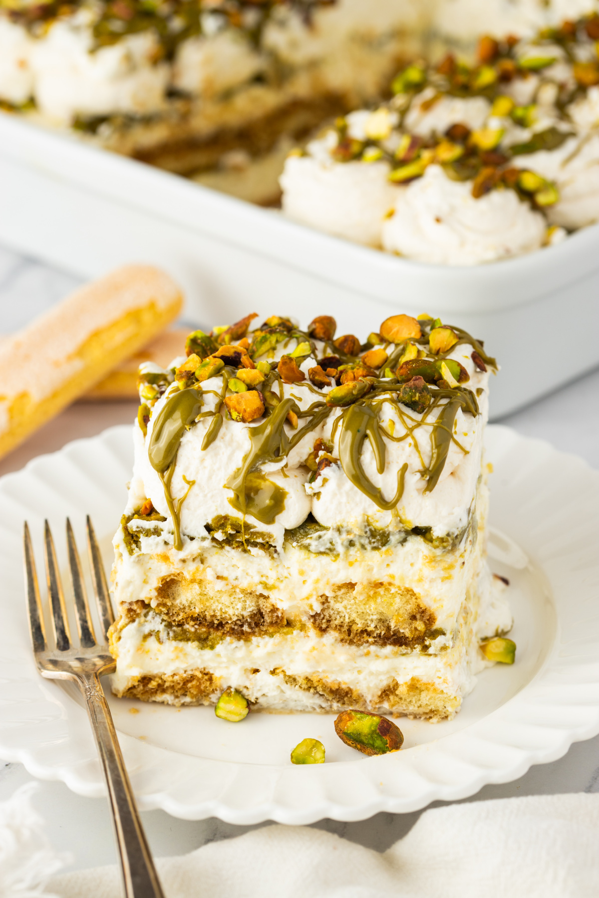 pistachio tiramisu slice with layers of mascarpone cream and espresso soaked ladyfingers topped with pistachio cream and chopped pistachios