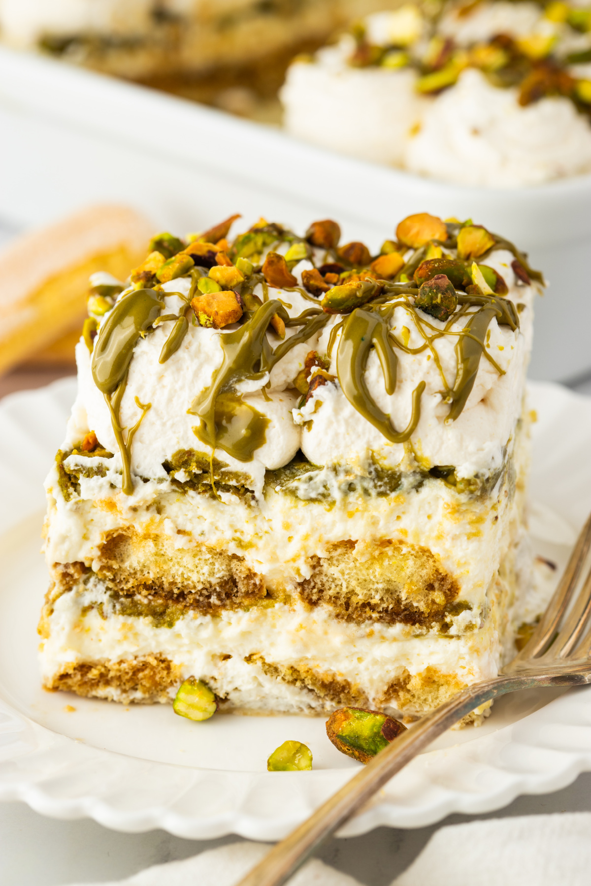 slice of tiramisu with mascarpone layers espresso soaked ladyfingers pistachio cream drizzle and chopped pistachios on top