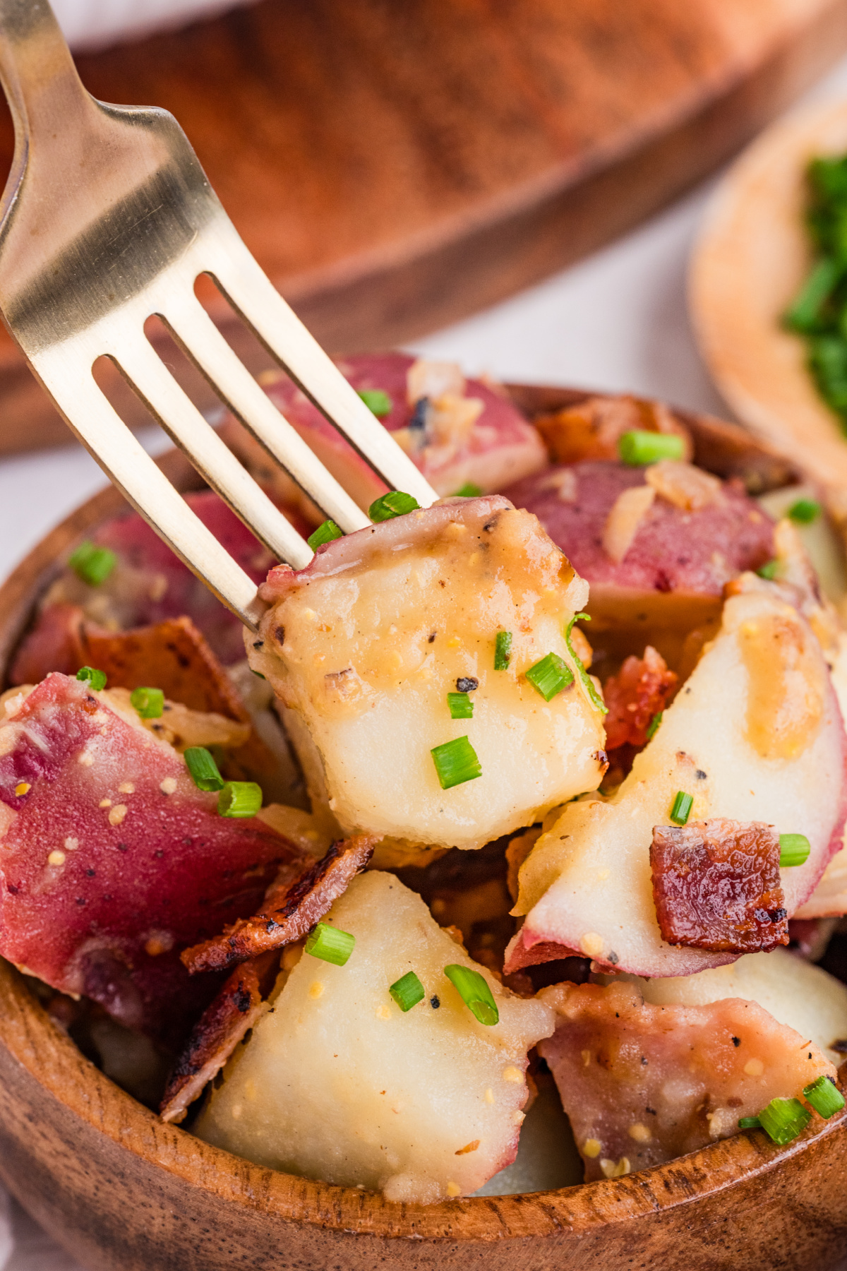 fork lifting red potato with bacon, mustard dressing, and chives from warm potato salad