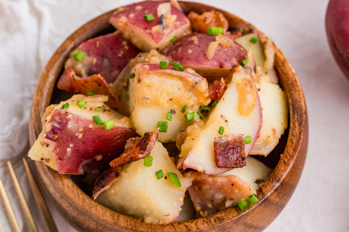 red potato salad with bacon, whole grain mustard dressing, and fresh chives in a wooden bowl