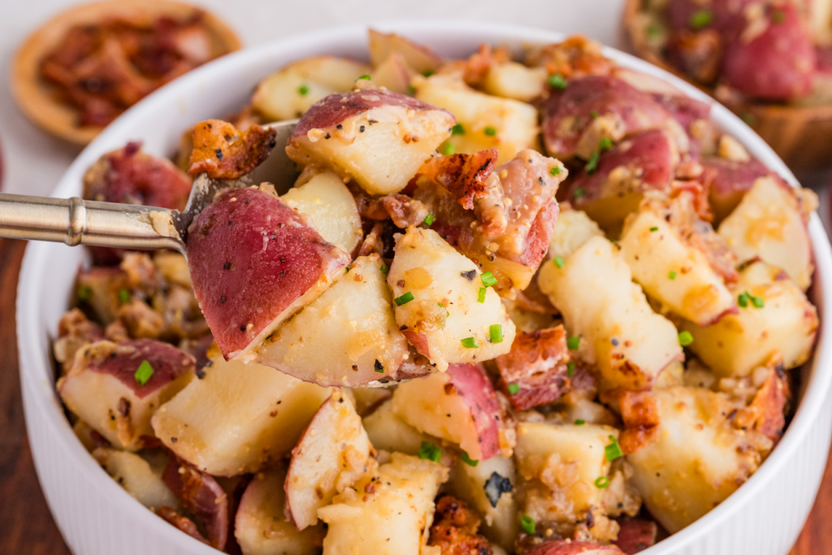 warm potato salad with bacon, red potatoes, and mustard dressing being served with a fork
