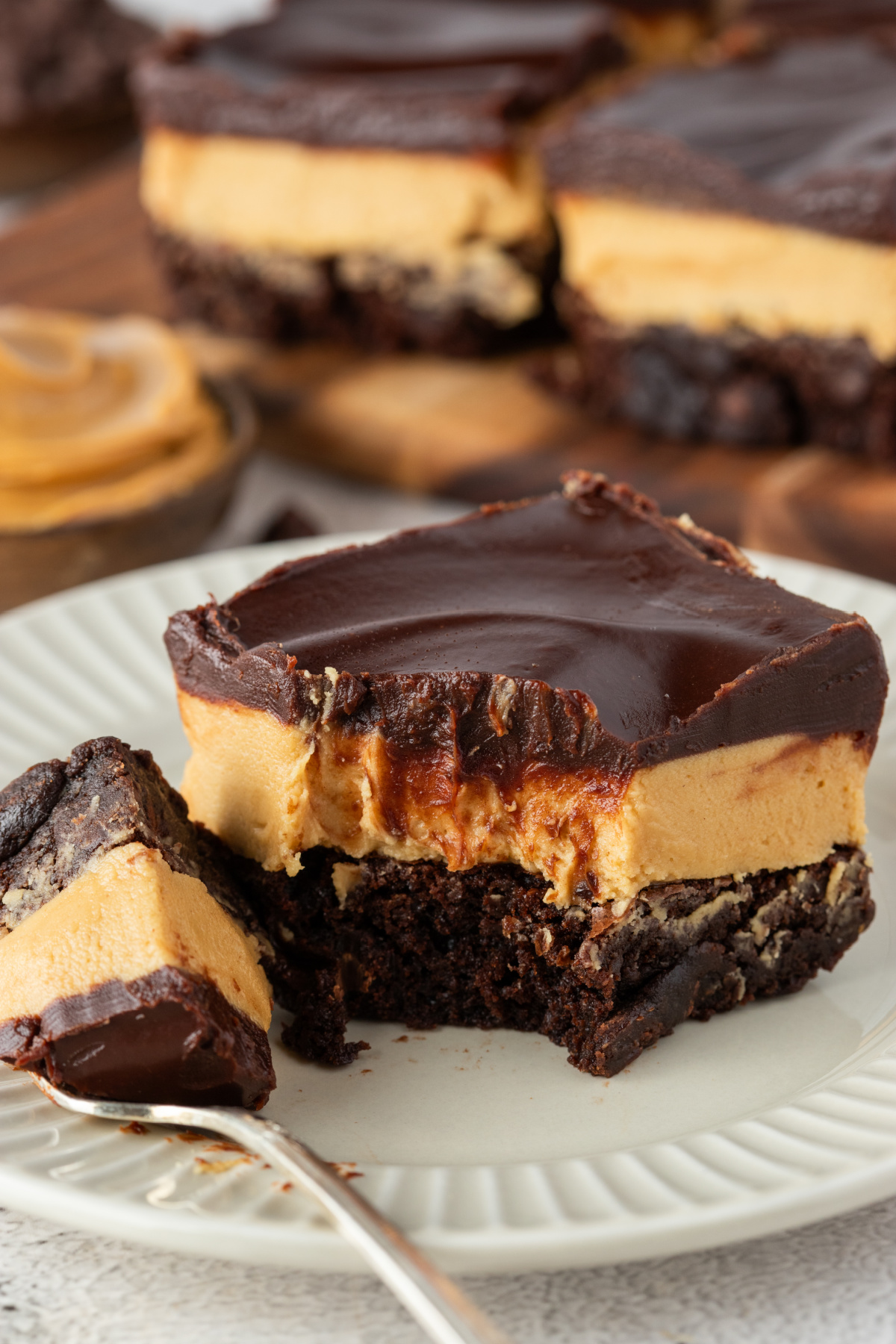 Buckeye brownies with a thick peanut butter filling, fudgy brownie base, and chocolate ganache topping on a plate