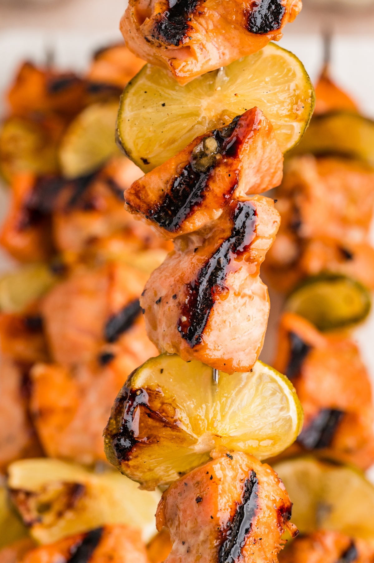 Close-up of grilled salmon skewers with caramelized glaze and charred lime slices threaded between the salmon pieces.