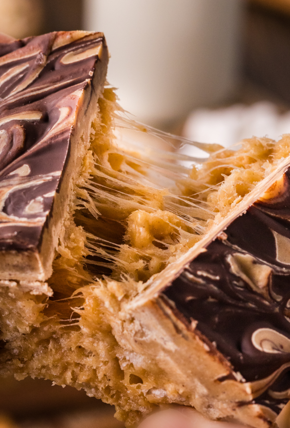 Close-up of chewy peanut butter marshmallow bars being pulled apart with melted marshmallow strands and chocolate swirls