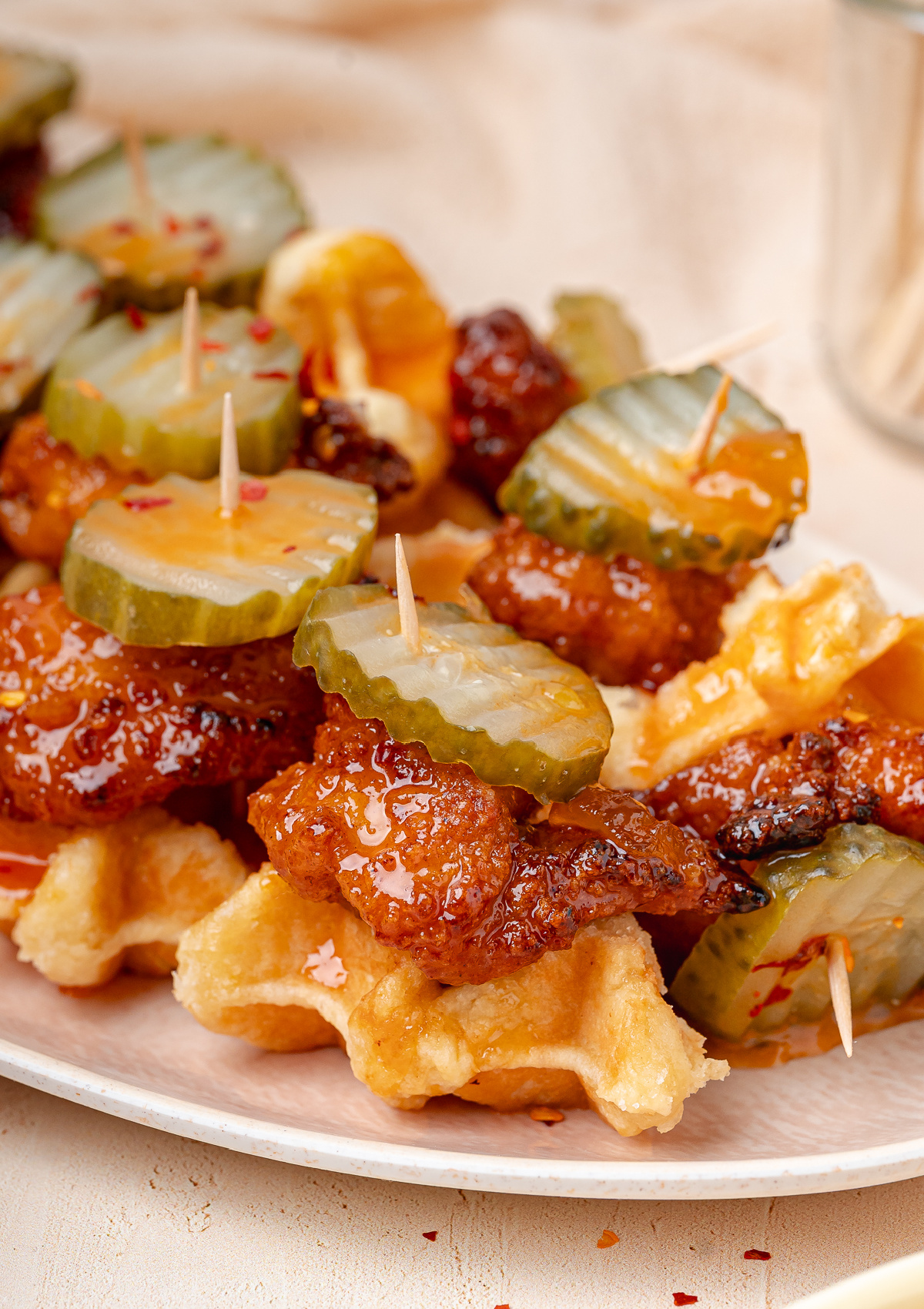 Chicken and Waffle Appetizer Close-Up Chicken and waffle appetizer topped with glazed chicken, dill pickle chips, and peach hot honey sauce.