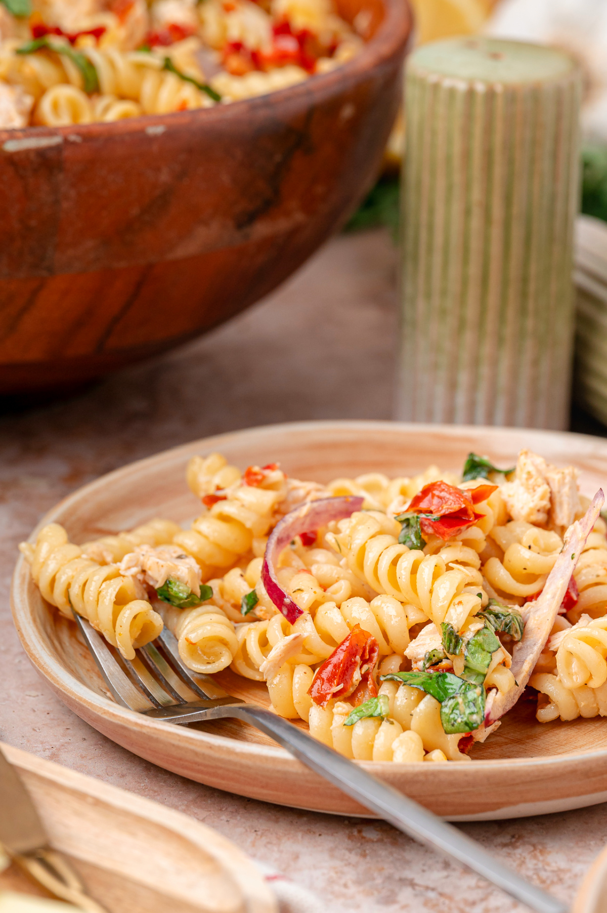 Chicken pasta salad with rotini, basil, red onion, and sun-dried tomatoes served on a small plate