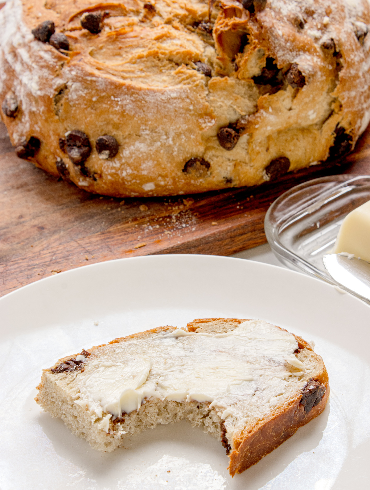 slice of chocolate chip bread with butter and a bite taken on a white plate