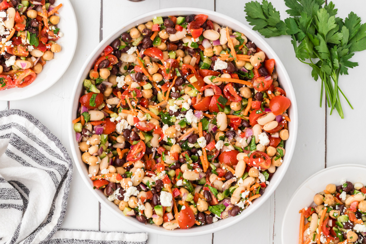 Large bowl of chopped bean salad with feta cheese, fresh vegetables, and lemon Dijon dressing ready for meal prep lunches. Chopped bean salad with feta cheese, chickpeas, black beans, cannellini beans, tomatoes, cucumber, and parsley