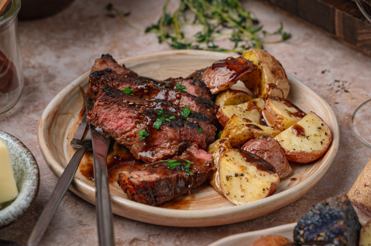 Cocoa crusted steak with stout pan sauce served with roasted potatoes on a ceramic plate.
