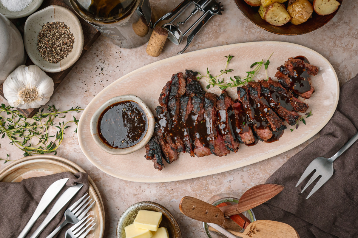 Cocoa rubbed steak with dark stout pan sauce sliced on a serving platter with extra sauce on the side.