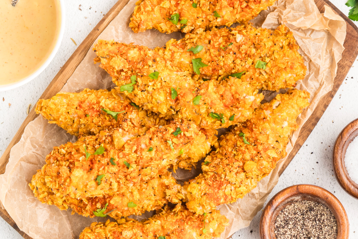 Overhead view of Cornflake Crusted Chicken Tenders with crispy jagged cornflake coating on a parchment-lined wooden board