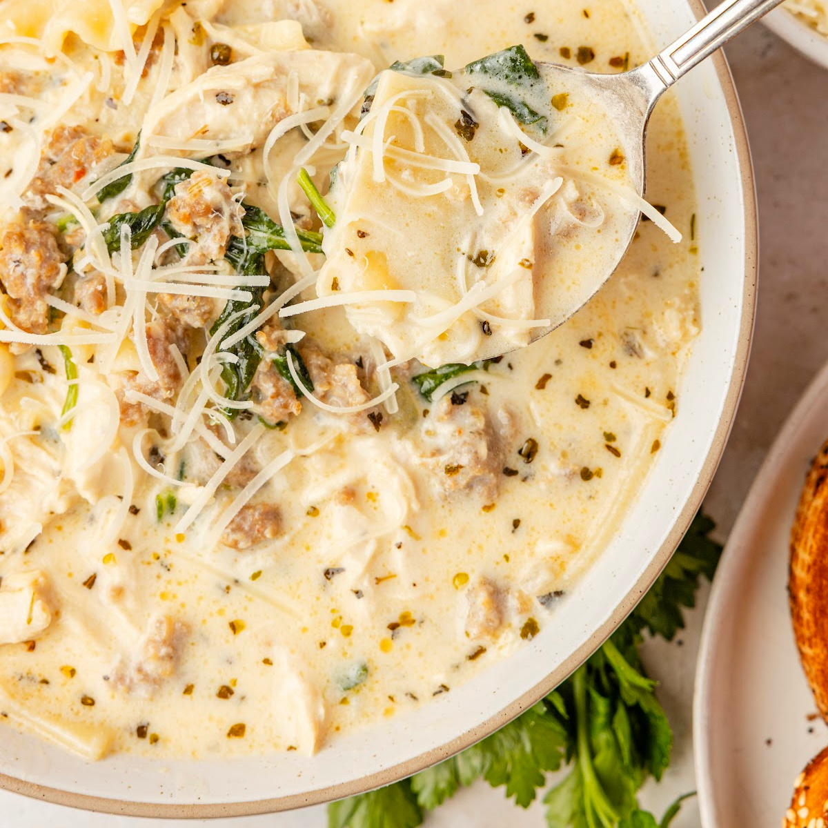 White Lasagna Soup made with sausage, chicken, ricotta, mozzarella, spinach, and broken lasagna noodles in creamy broth
