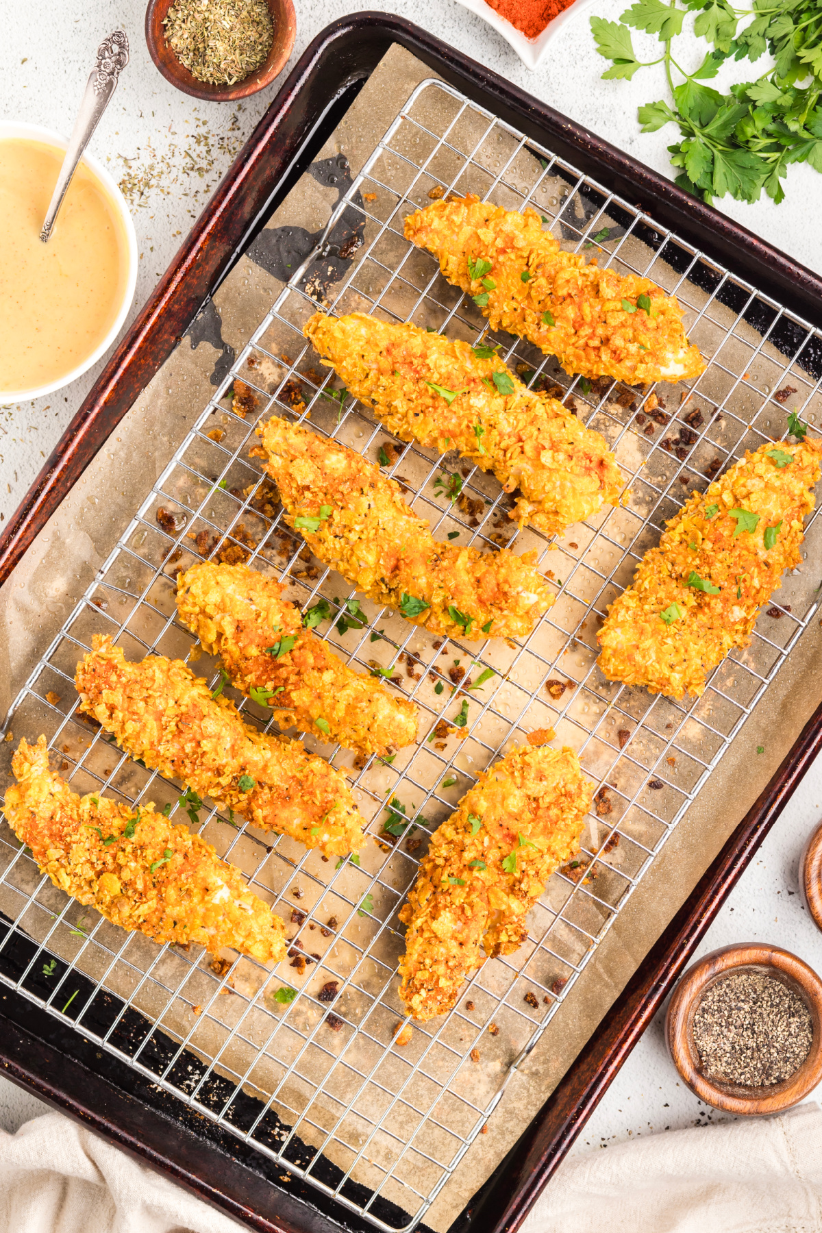 Crispy baked chicken tenders with cornflake coating cooling on a wire rack over a sheet pan