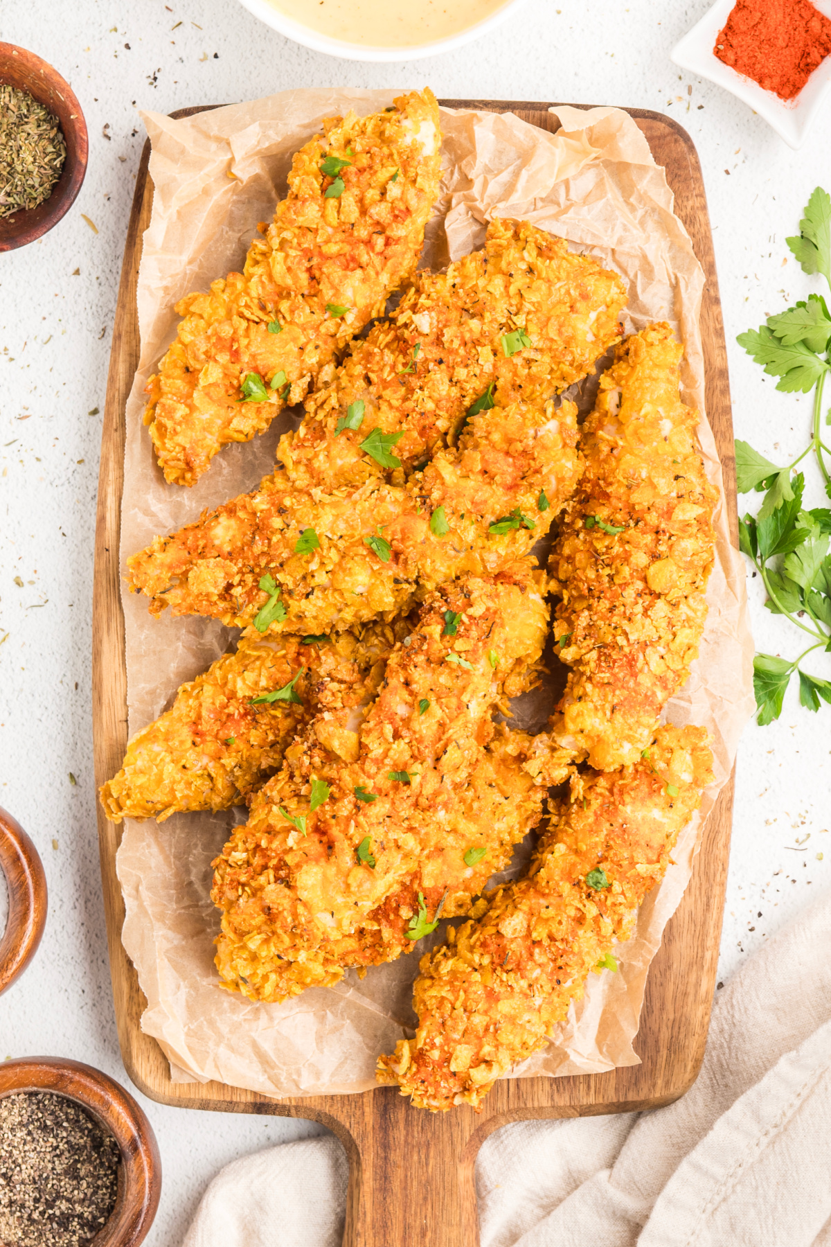 Overhead photo of crispy baked chicken tenders with thick cornflake crust on a wooden serving board