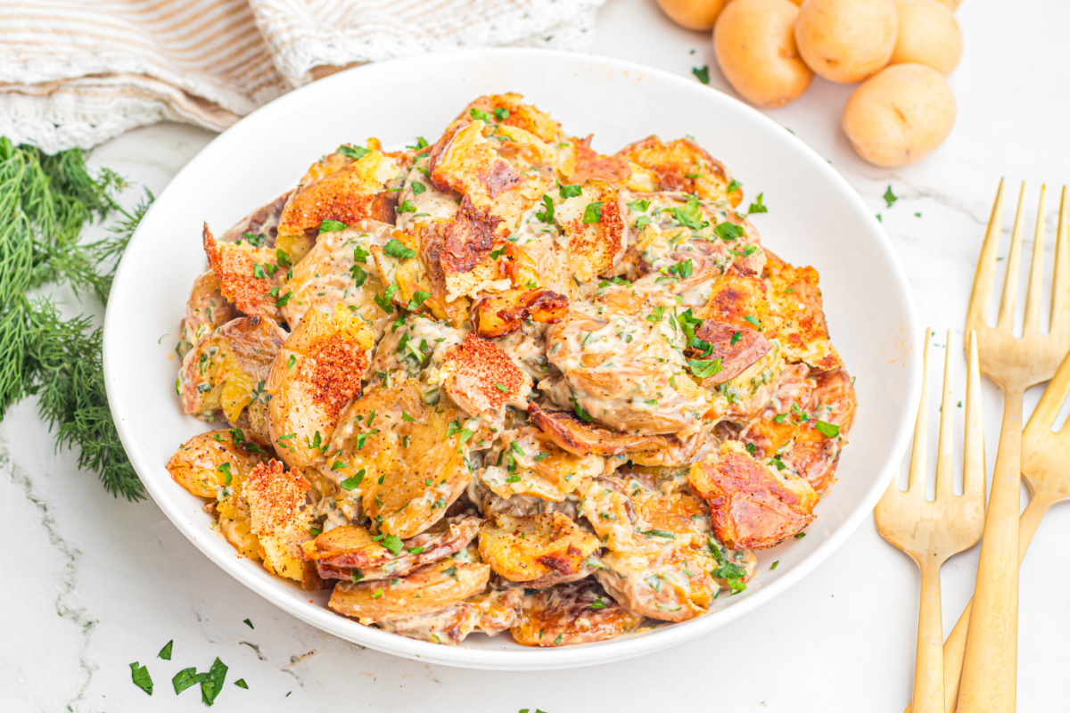 Crispy Smashed Potato Salad in a white bowl with roasted baby potatoes, creamy lemon herb dressing, fresh dill, parsley, and crispy golden potato edges
