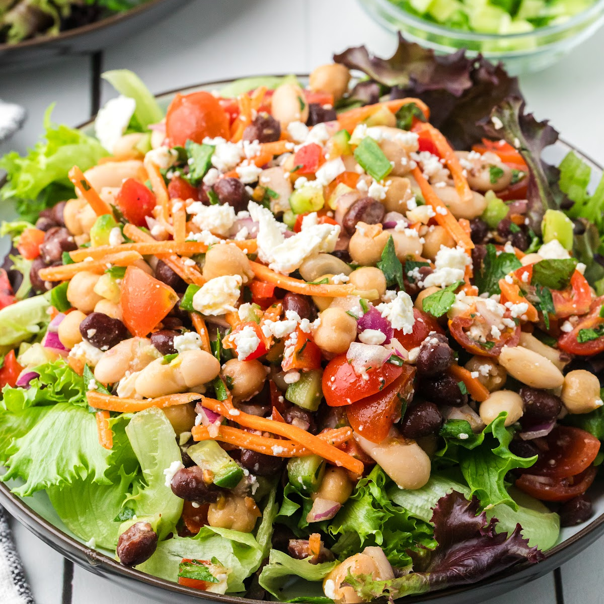 Dense bean salad with lemon Dijon dressing served over lettuce with feta cheese, chickpeas, black beans, cannellini beans, and chopped vegetables