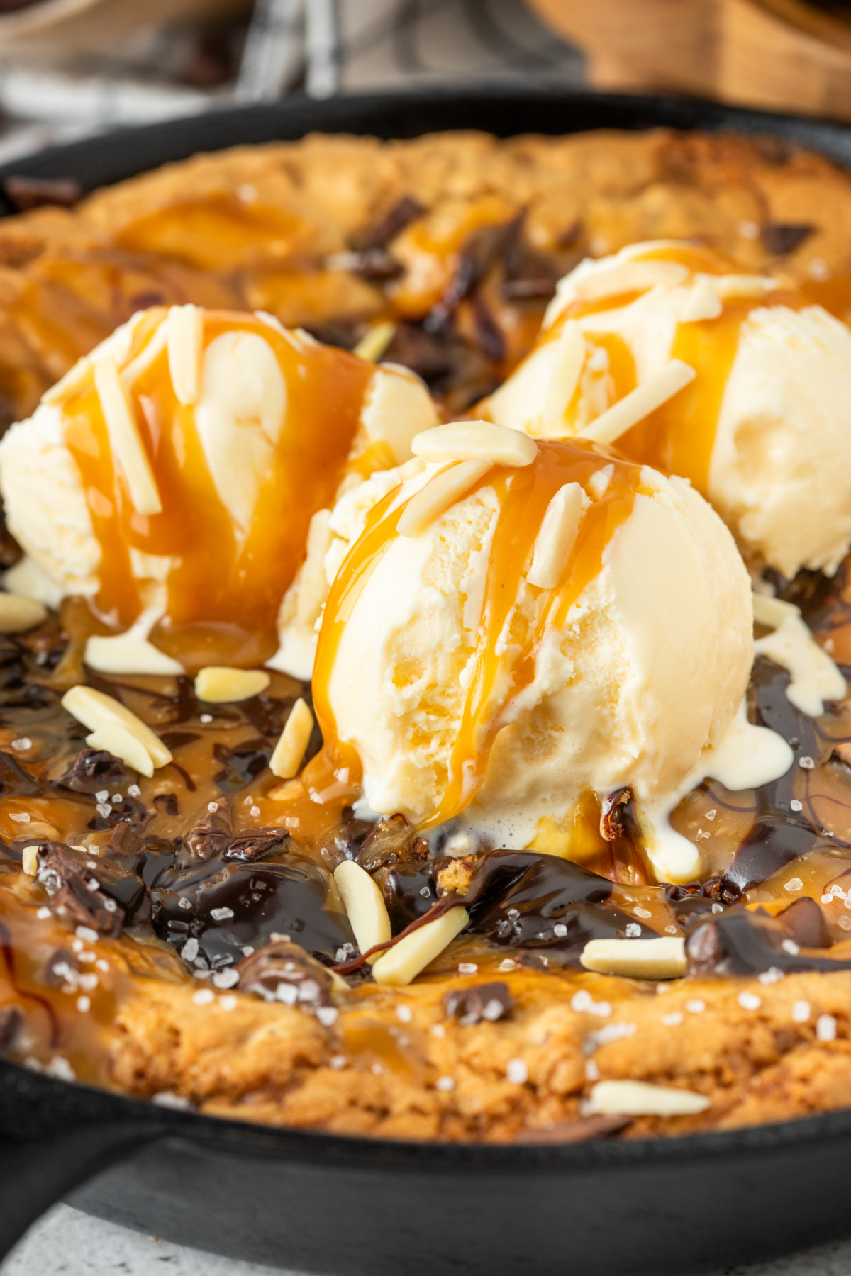 Gooey salted caramel skillet cookie topped with melting vanilla ice cream, caramel sauce, chocolate drizzle, flaky sea salt, and chocolate chunks in a cast iron skillet.