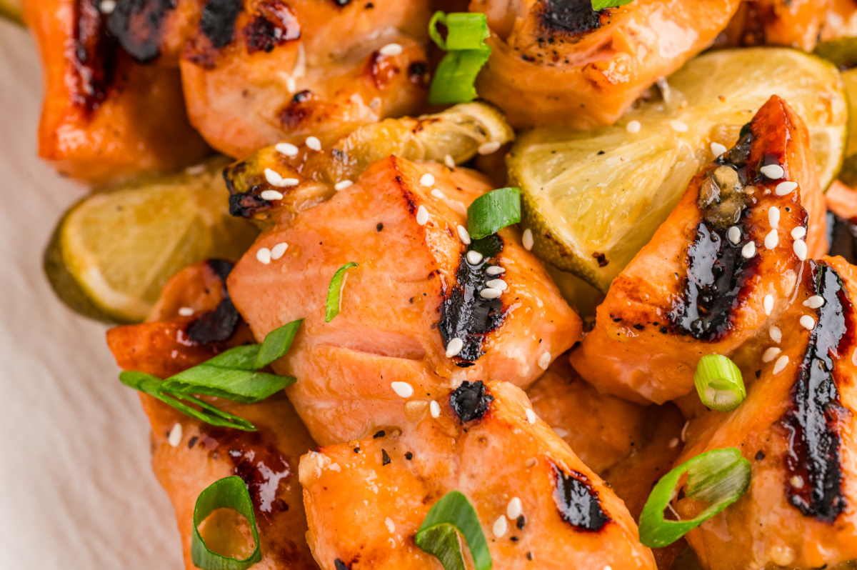 Close-up of grilled honey soy lime salmon skewers with smoky charred edges and grilled lime. Close-up of grilled honey soy lime salmon skewers with caramelized char, sesame seeds, green onions, and grilled lime slices.