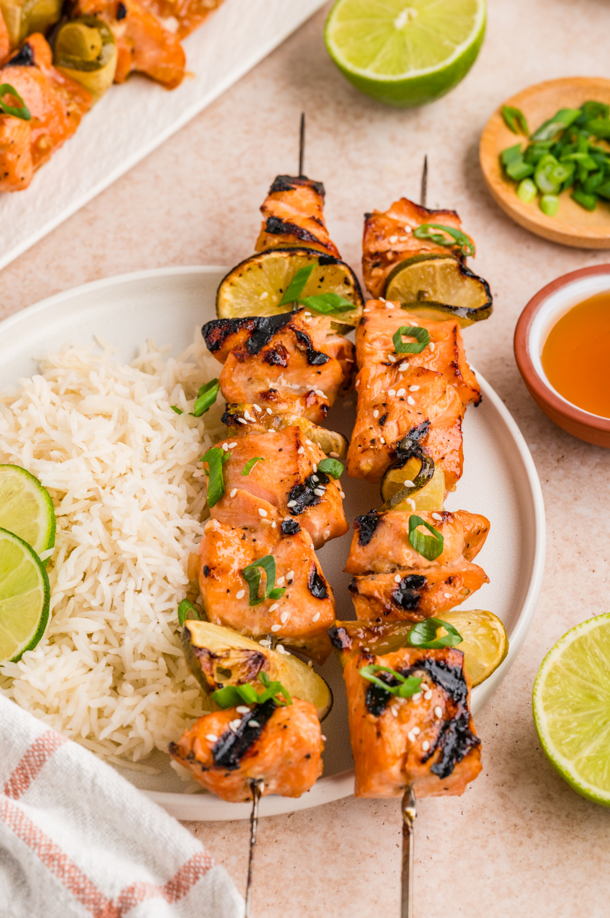 Grilled honey soy lime salmon skewers with caramelized edges and charred lime served over rice. Grilled honey soy lime salmon skewers served with white rice, charred lime slices, sesame seeds, and green onions on a dinner plate.
