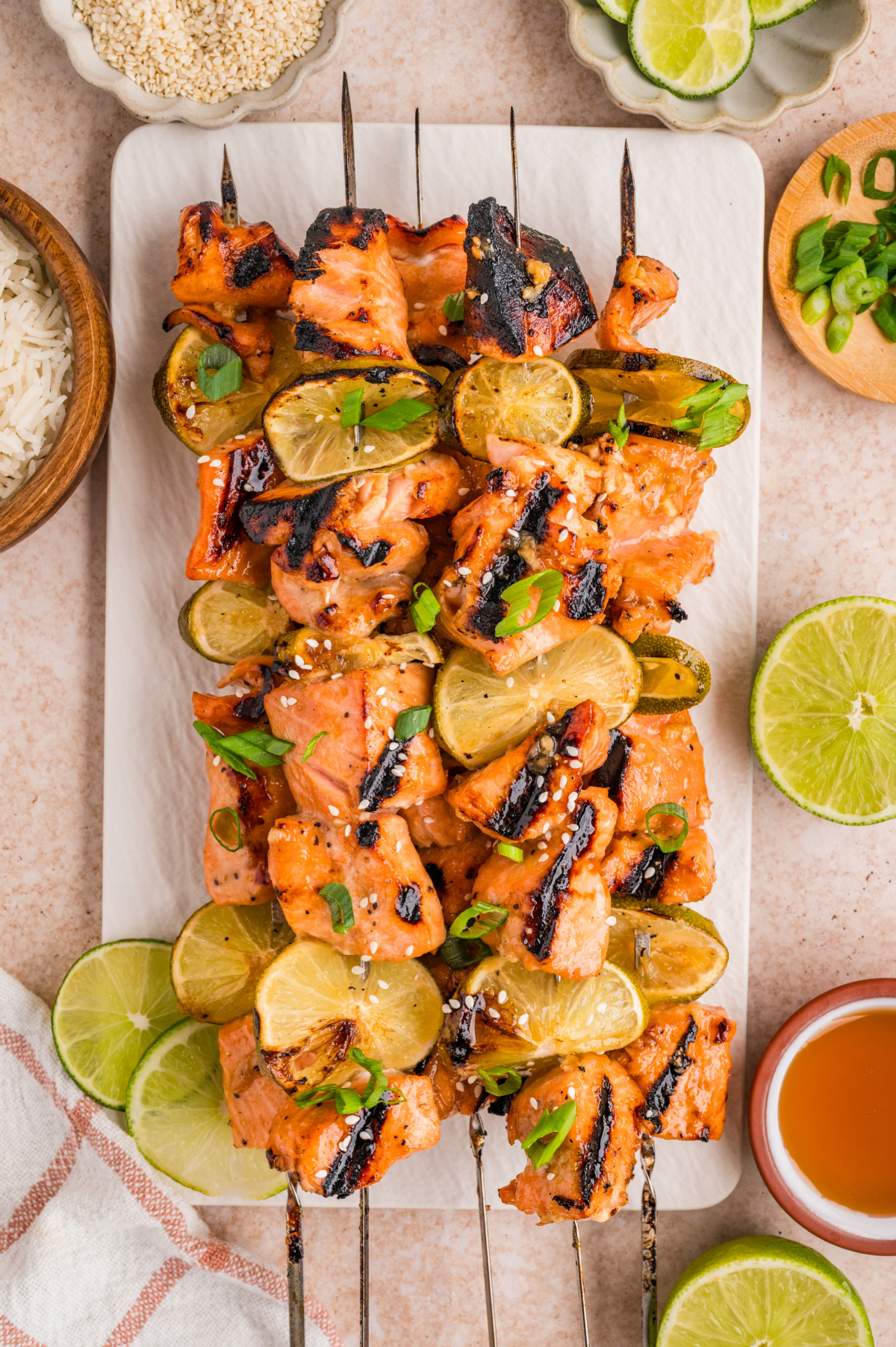 Grilled honey soy lime salmon skewers on a serving platter with charred lime slices, sesame seeds, and green onions.
