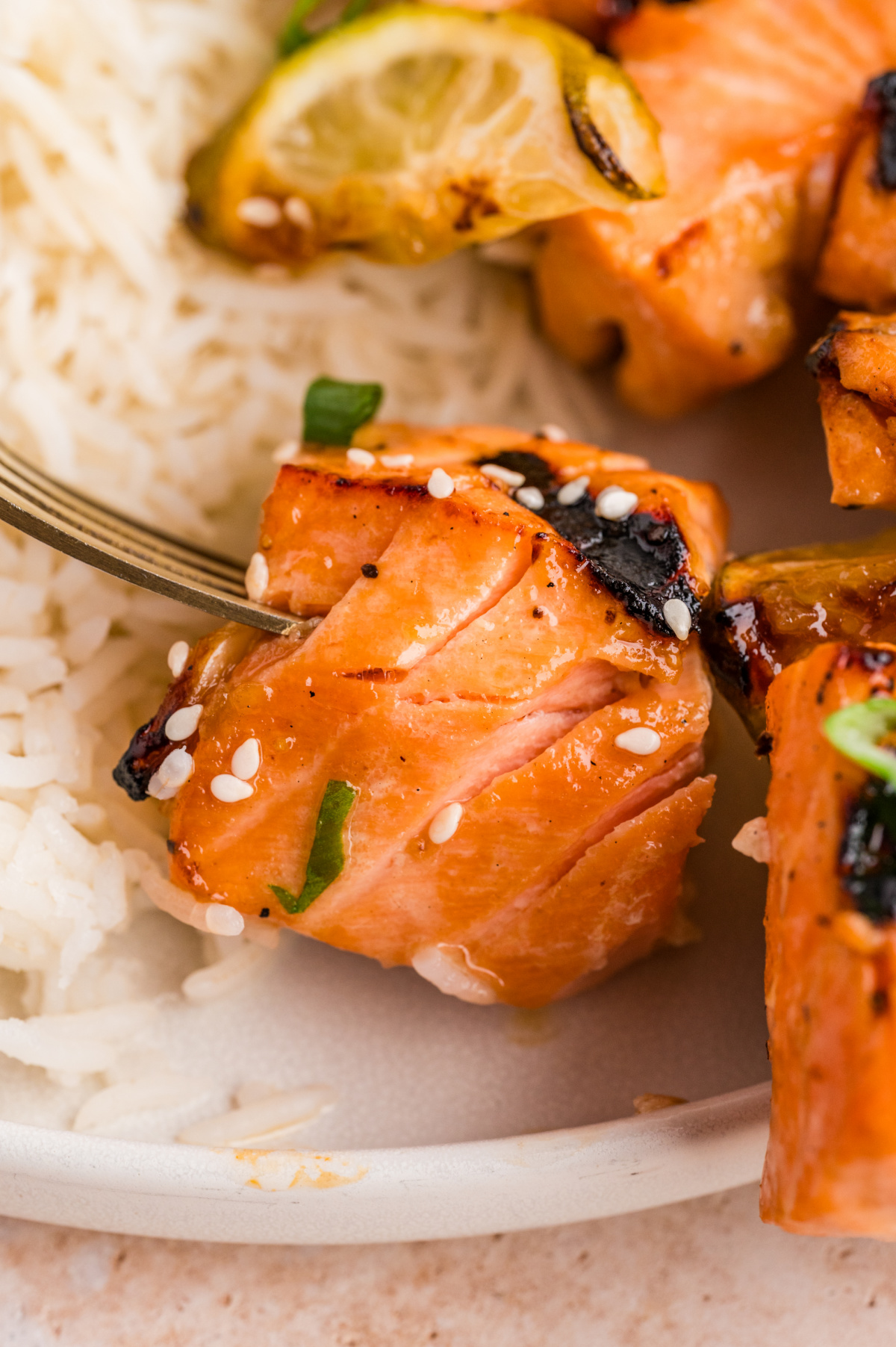 Close-up of grilled salmon skewers showing the flaky salmon center with caramelized glaze, sesame seeds, and grilled lime.