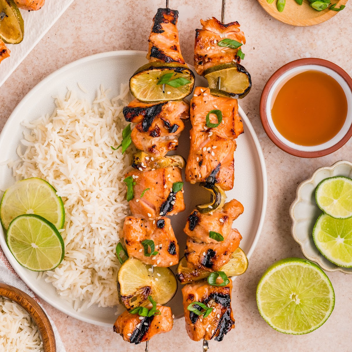 Overhead view of grilled honey soy lime salmon skewers with white rice, charred lime, sesame seeds, and sliced green onions
